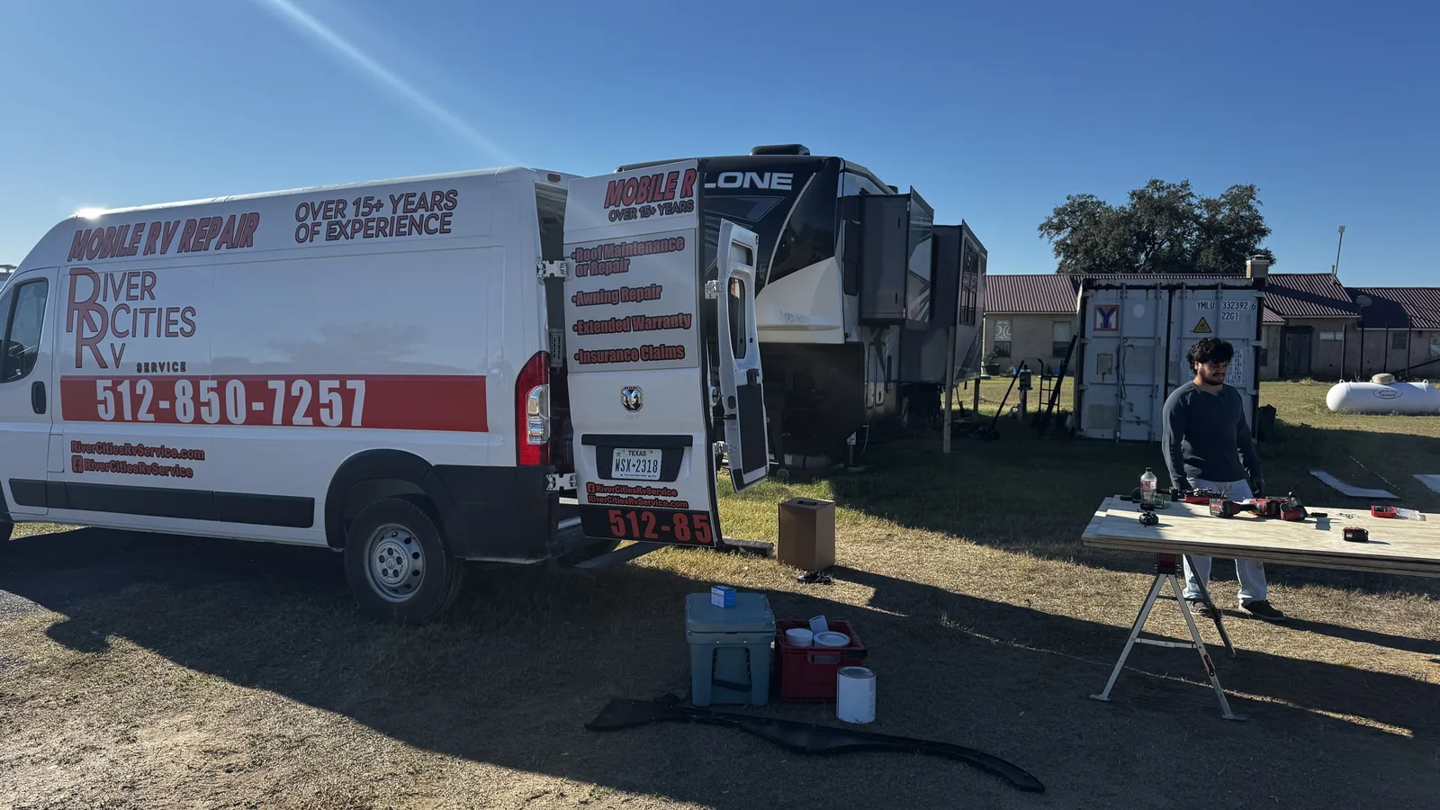 River Cities RV Service van parked beside a fifth wheel at an RV park with a technician working at a folding table, mobile RV repair