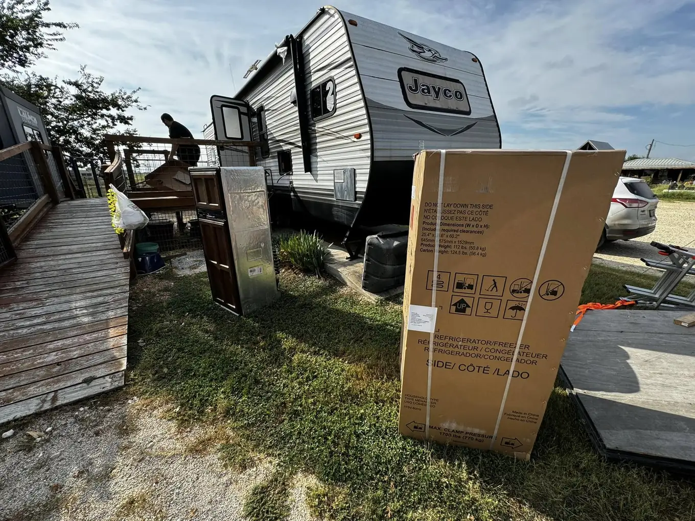 Boxed replacement refrigerator beside a travel trailer at an RV park, RV refrigerator repair