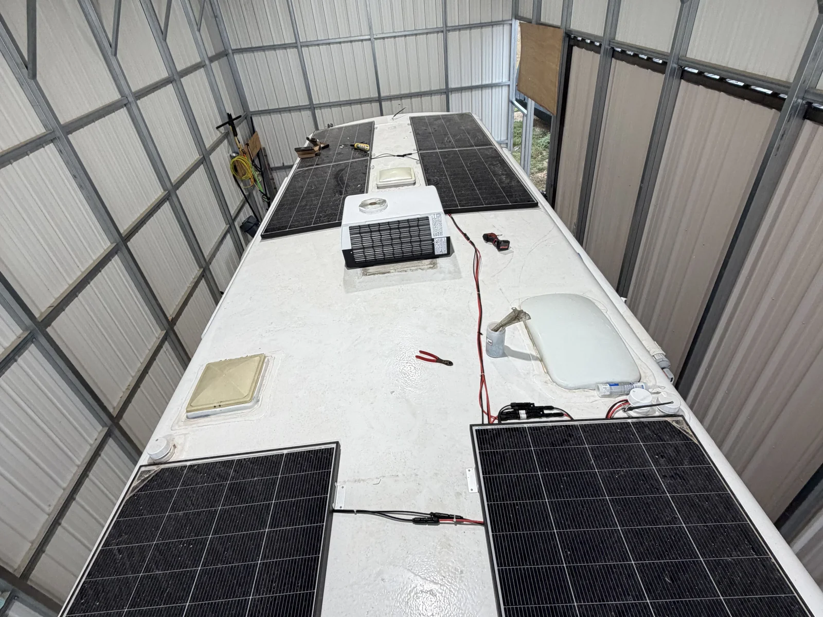 Three solar panels wired on the roof of a travel trailer parked under a carport, RV solar and electrical work