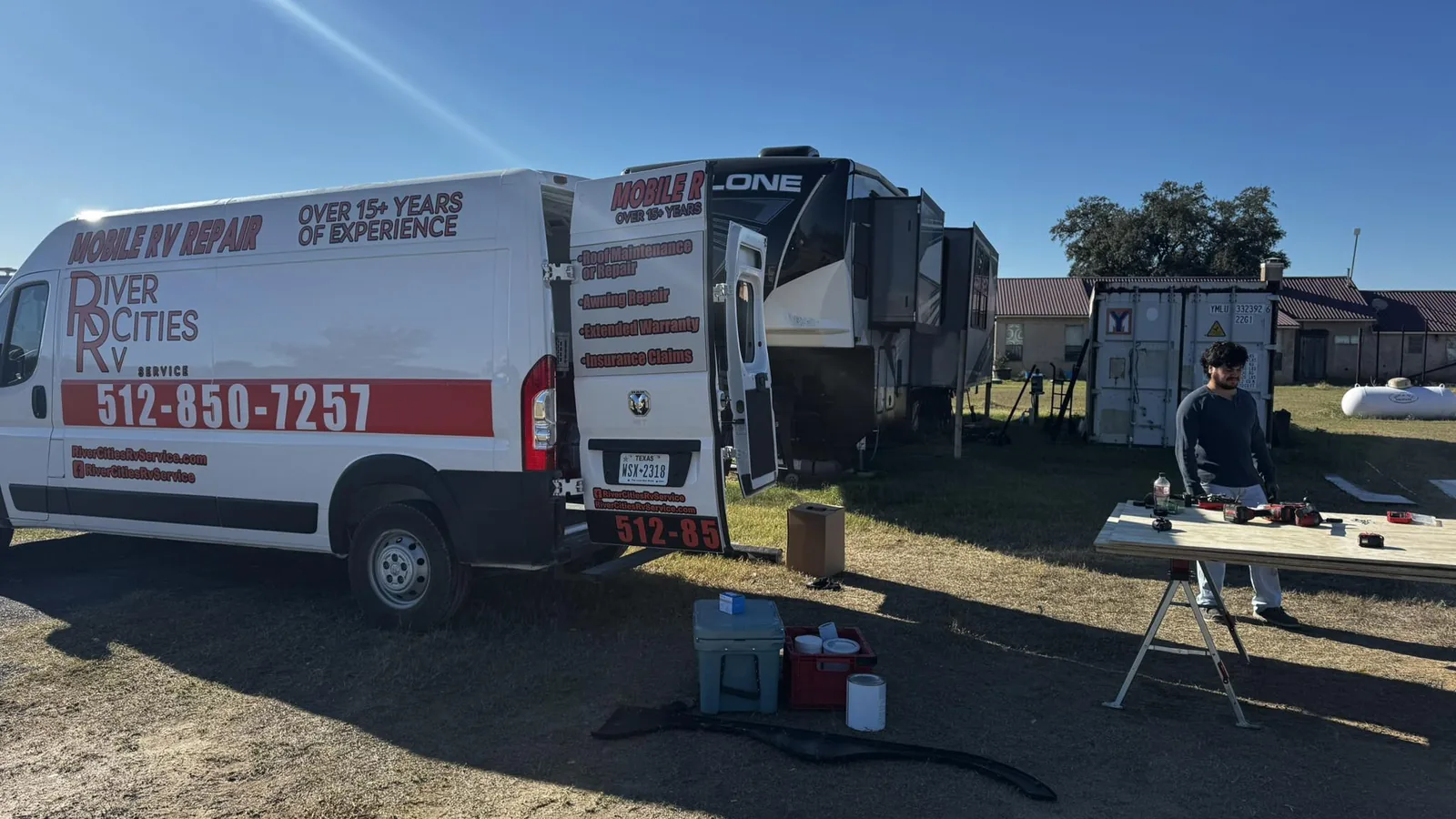 River Cities RV Service van beside a fifth wheel at an RV park with a technician at a work table, mobile RV repair
